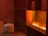 A room with warm lighting features a modern fireplace with visible flames. In the foreground, there's a round houndstooth-patterned pouf next to a dark wooden side table. The wall and shelving unit is composed of dark wood, adding to the cozy and intimate ambiance.