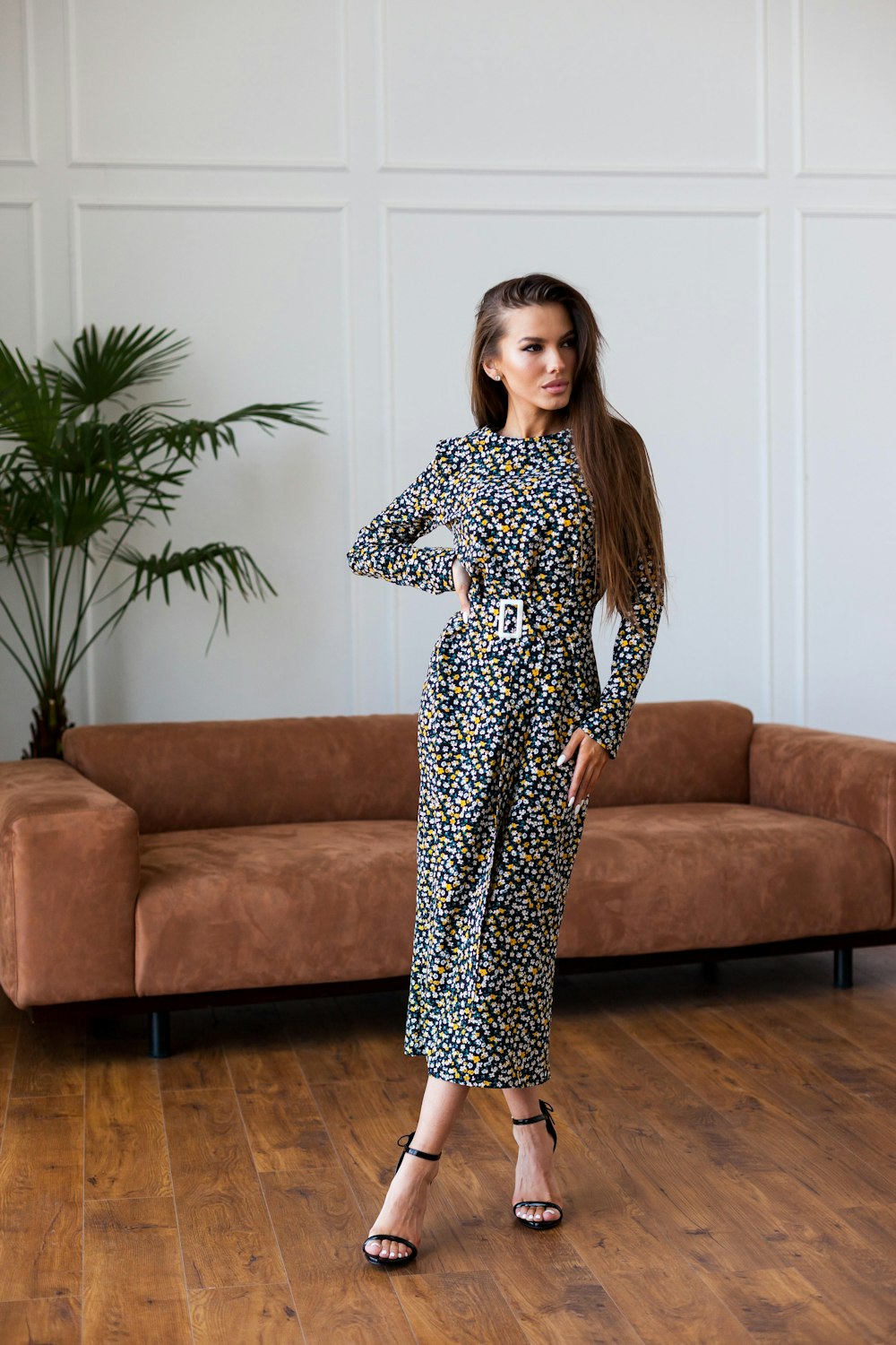 woman in black and white floral long sleeve dress standing beside brown couch