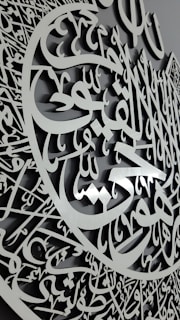 A detailed carving featuring intricate Arabic calligraphy with an elegant script and a three-dimensional appearance. The calligraphy is arranged in a circular pattern, suggesting a decorative and artistic design.