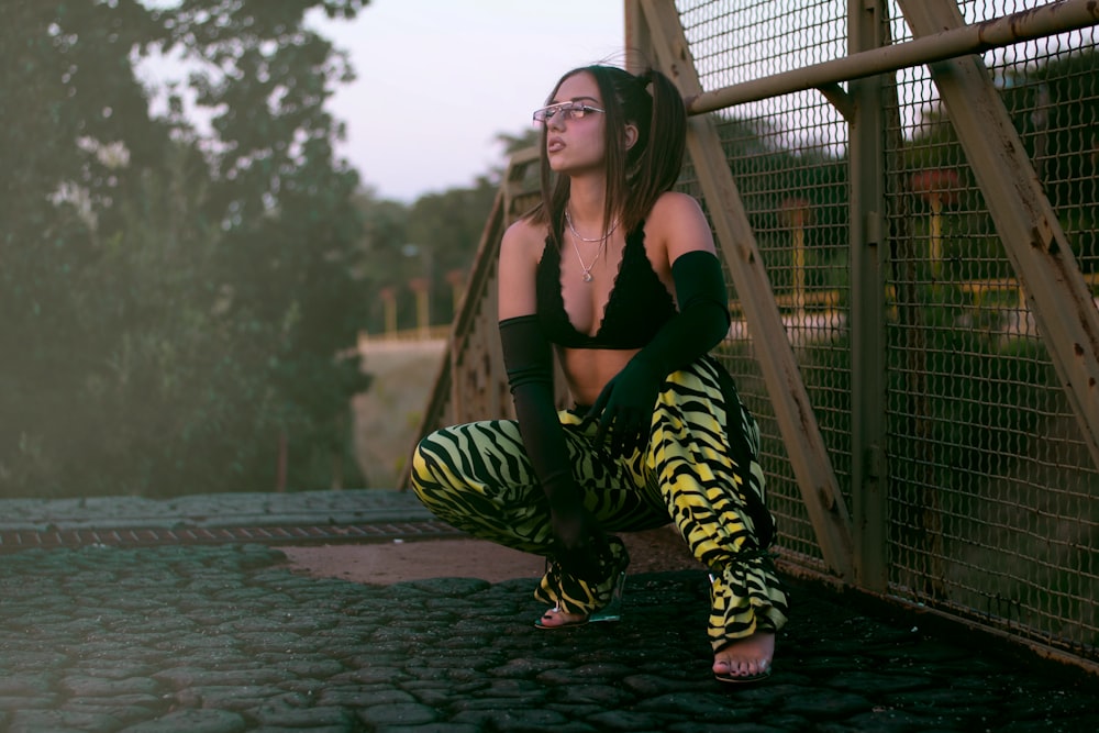 woman in black and white zebra print pants sitting on brown wooden dock during daytime