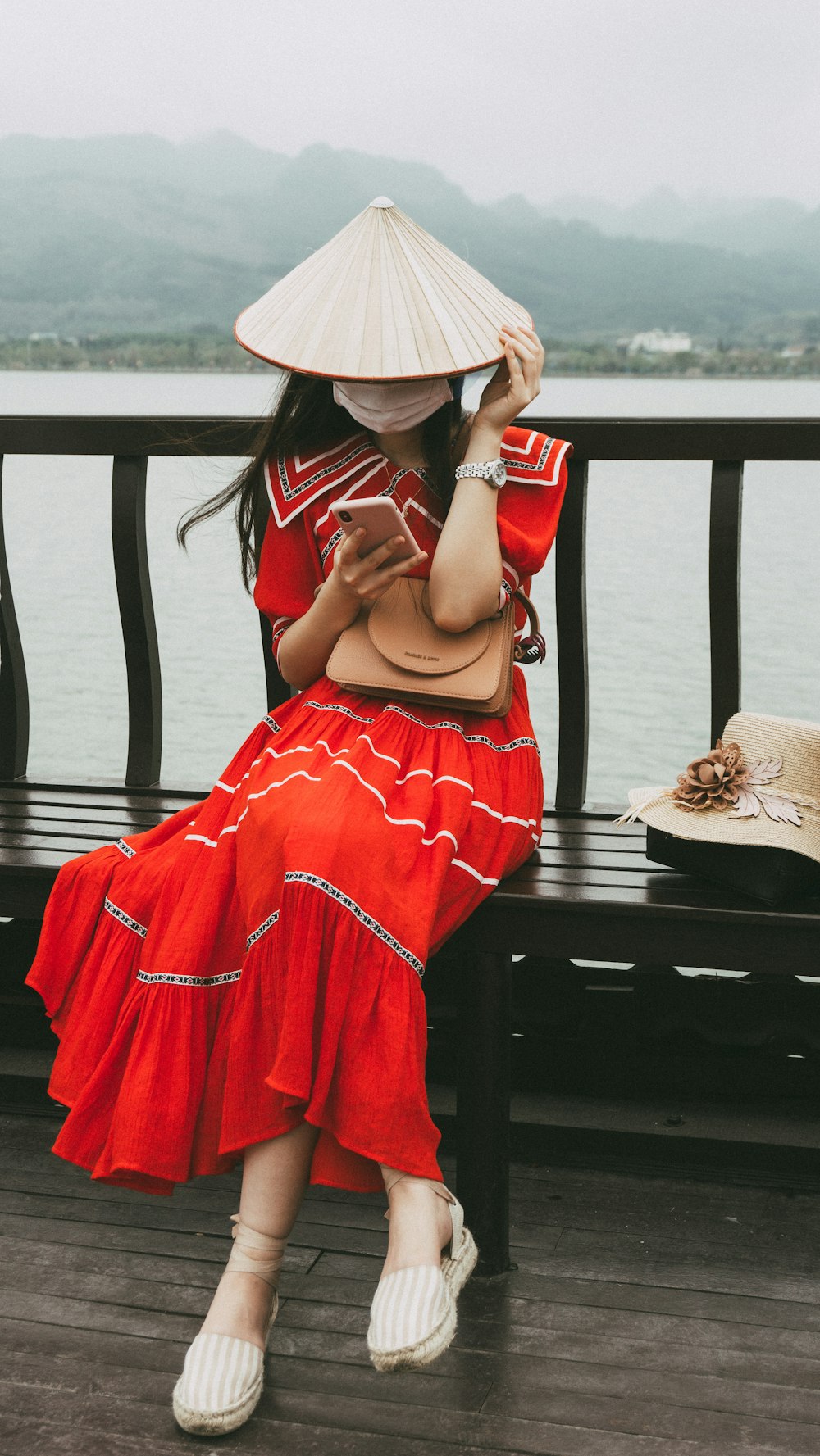 woman in red dress wearing white sun hat sitting on brown wooden bench during daytime