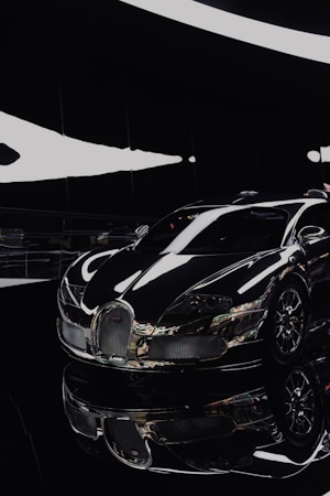 A sleek, luxury sports car with a glossy black finish is prominently displayed in a modern, well-lit showroom. The car's smooth curves and shiny chrome accents reflect light, adding to its futuristic and high-end appearance. The setting is minimalistic, enhancing the car's striking design.