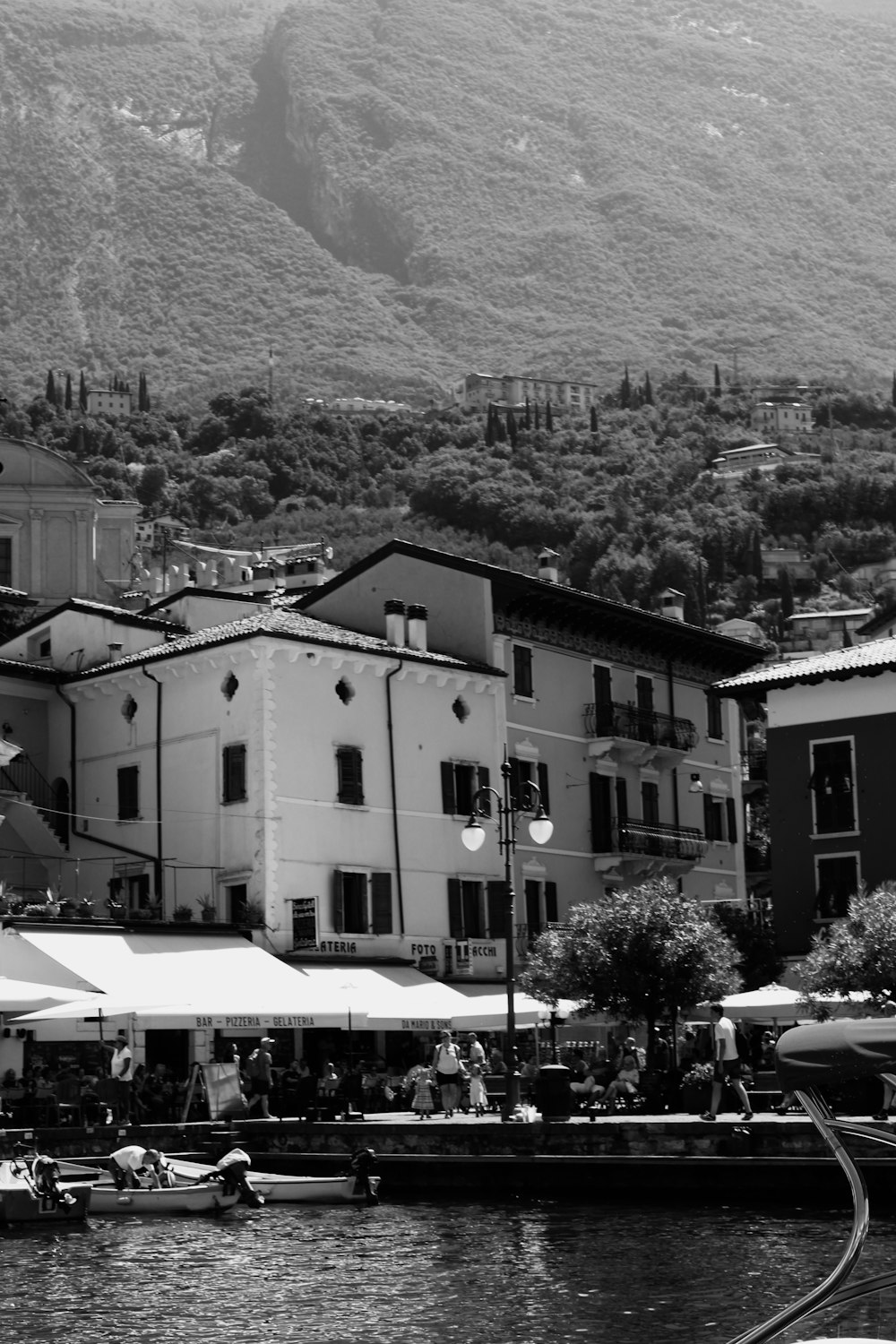 grayscale photo of people walking on street near buildings and trees