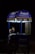 A person is sitting inside a small mobile ice cream cart with the Amul logo prominently displayed. The cart is primarily blue and purple with illuminated signs, and the person appears to be on a phone call. The setting seems to be dark, possibly at night, with the cart lit up against the surrounding darkness.