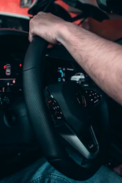 Close-up of hands on a steering wheel with a dashboard showing modern car controls.