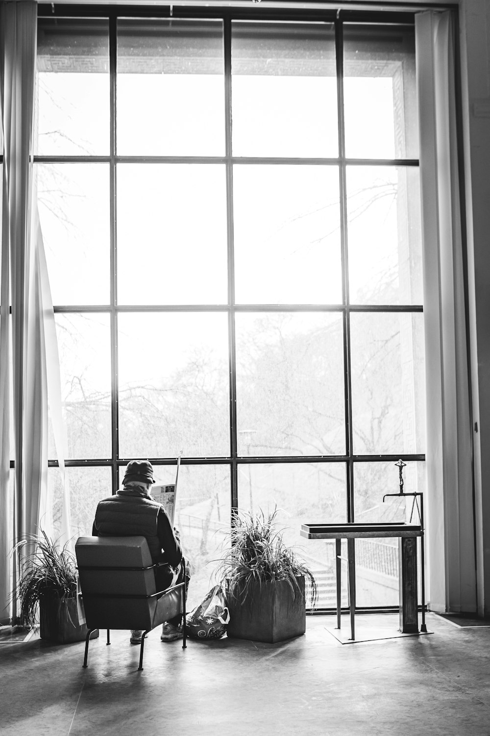 grayscale photo of woman sitting on chair in front of window