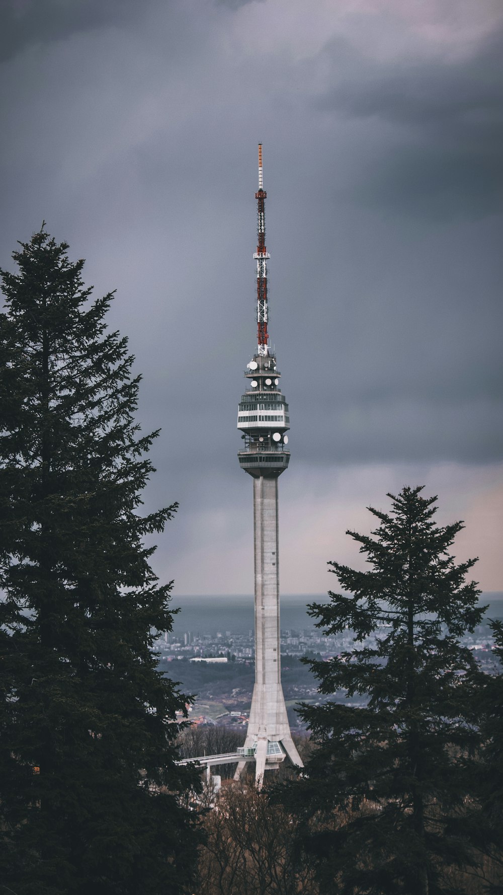 white and red tower near green trees under gray sky