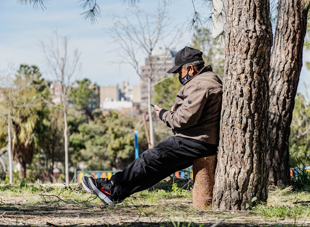 man in brown jacket and blue denim jeans sitting on brown tree trunk during daytime