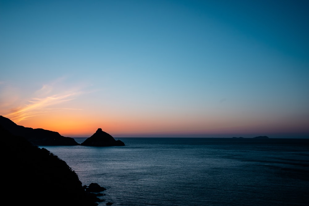 silhouette of mountain beside sea during sunset