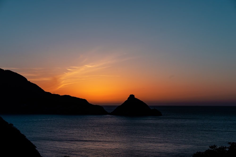 silhouette de montagne sur plan d’eau au coucher du soleil