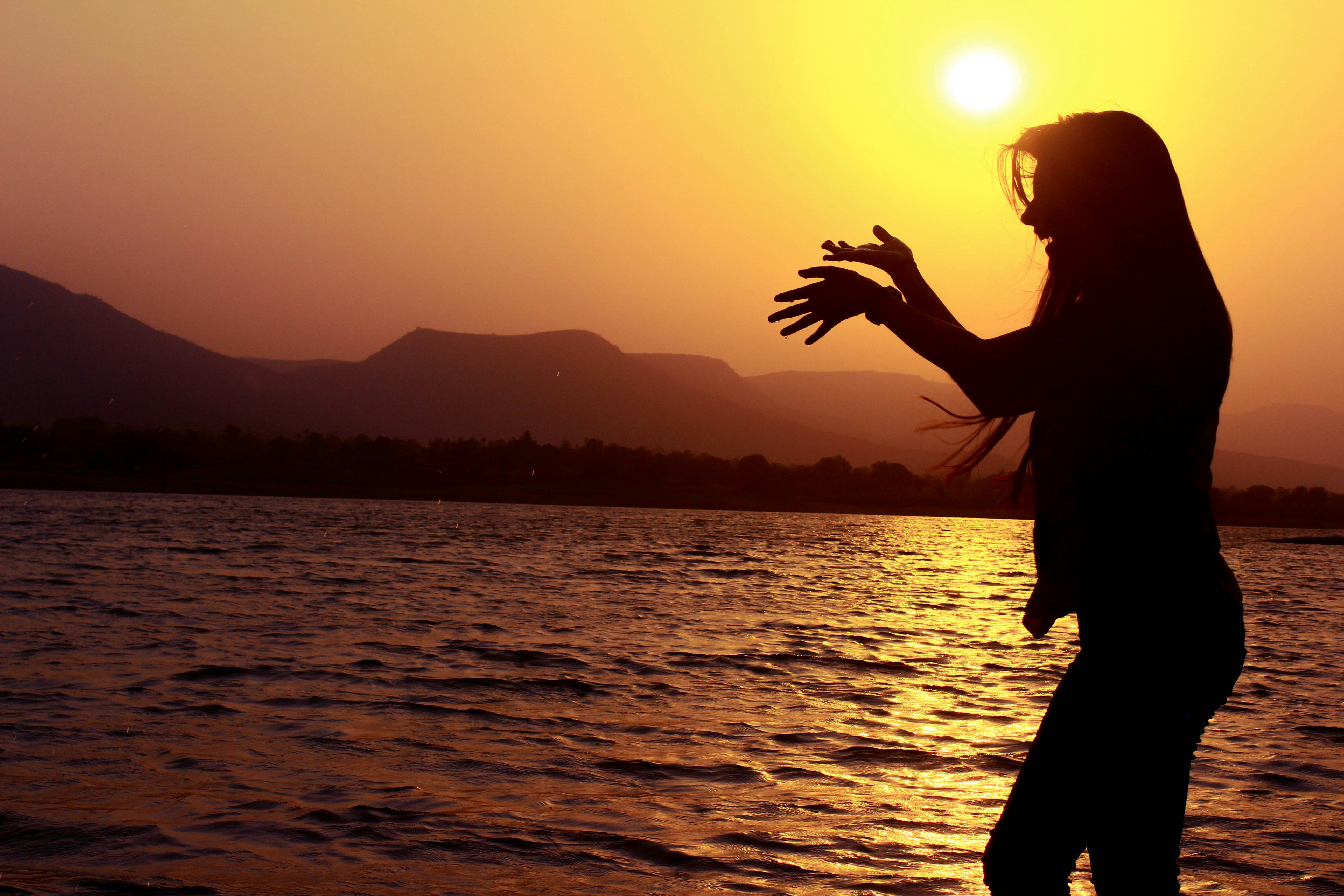 silhouette of woman standing near body of water during sunset