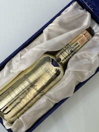 A golden-colored whisky bottle labeled 'Canadian Club' rests in a plush, white fabric lining within a navy blue box. The text 'IMPORTED' is prominently displayed on the bottle along with intricate details and a date noted as 1971.