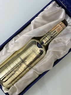 A golden-colored whisky bottle labeled 'Canadian Club' rests in a plush, white fabric lining within a navy blue box. The text 'IMPORTED' is prominently displayed on the bottle along with intricate details and a date noted as 1971.
