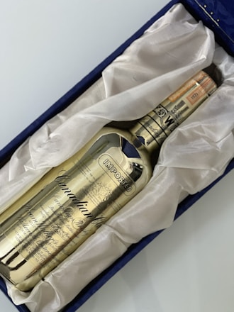 A golden-colored whisky bottle labeled 'Canadian Club' rests in a plush, white fabric lining within a navy blue box. The text 'IMPORTED' is prominently displayed on the bottle along with intricate details and a date noted as 1971.