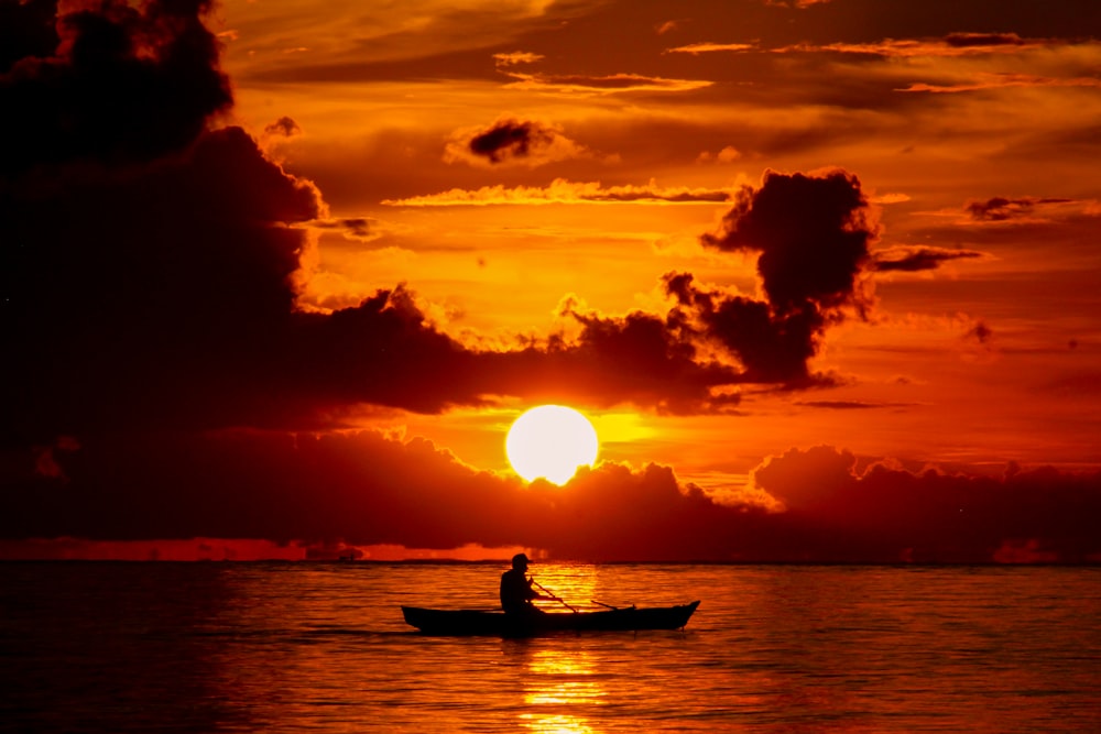 Silueta del hombre que monta en el barco durante la puesta del sol