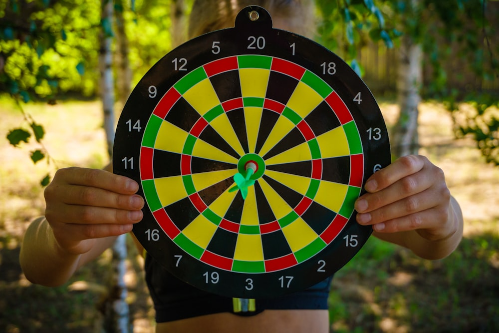 Persona che tiene l'orologio analogico rotondo nero, rosso, giallo e verde