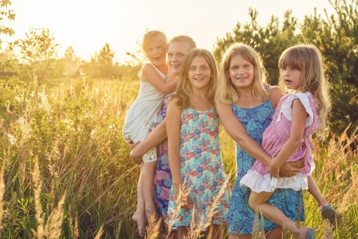 Mother and father with 3 girls standing on green grass field during daytime