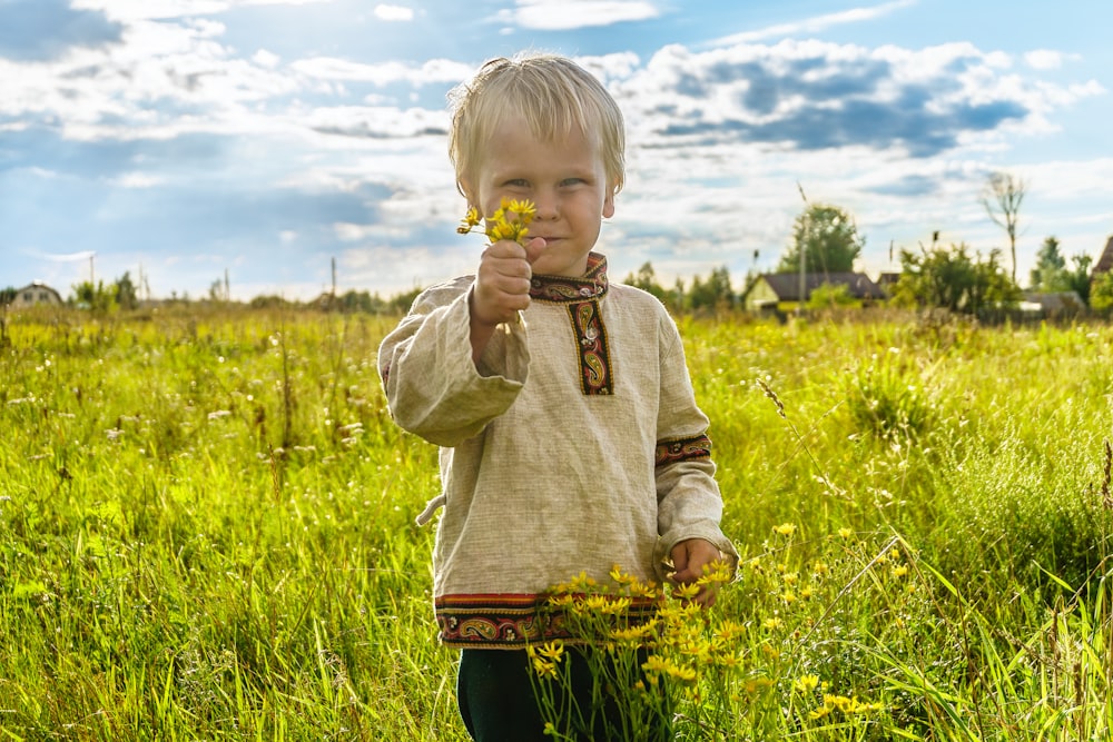 boy in gray sweater standing on green grass field during daytime