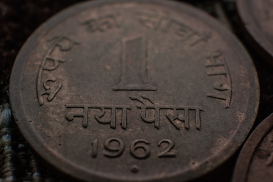 A close-up view of an old coin with Hindi script and the year 1962 etched on it. The coin appears to have some tarnish, indicating its age. The denomination is one 'Naya Paisa'.