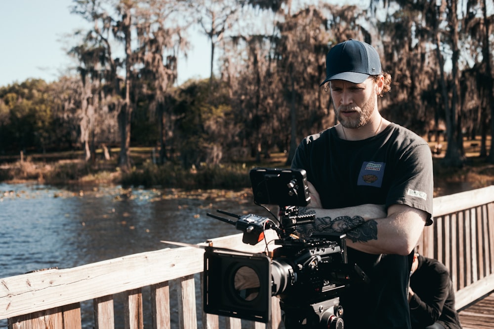 man in black polo shirt and blue cap holding black dslr camera