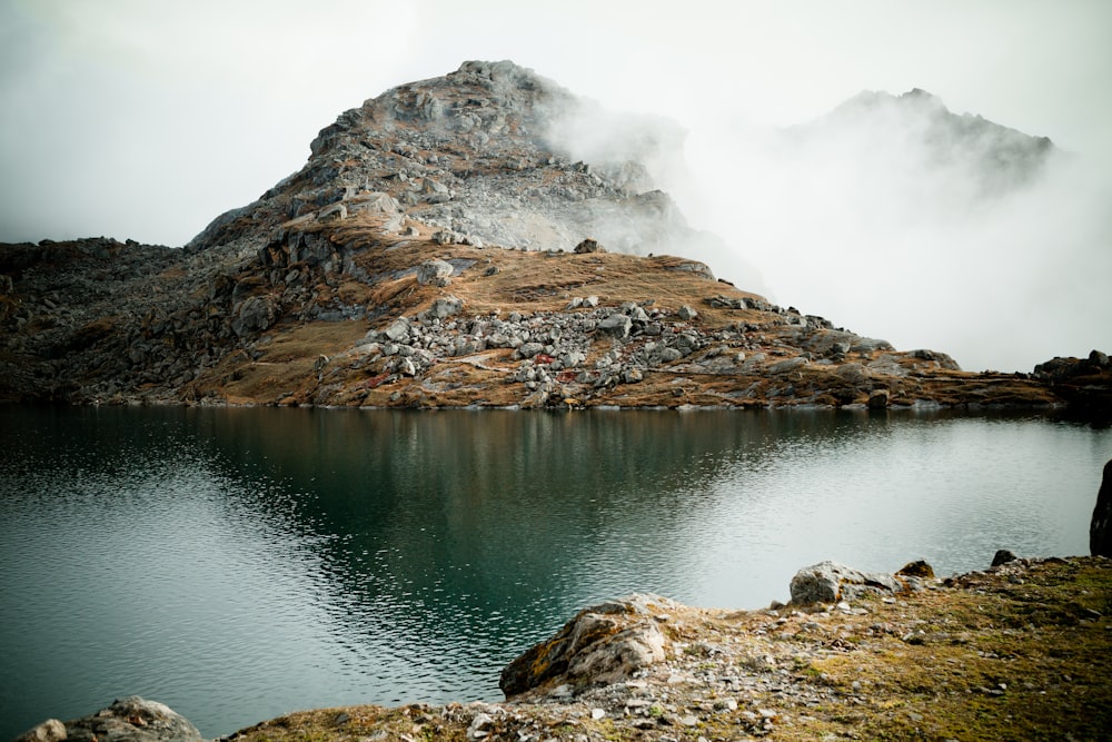 brown rocky mountain beside lake under white sky during daytime