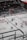 An ice hockey game taking place in an indoor arena with players wearing red and white uniforms on the ice. The rink is surrounded by glass panels, and there are spectators seated in the stands. A referee is visible on the ice, and advertisements line the perimeter of the rink.