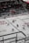 An ice hockey game taking place in an indoor arena with players wearing red and white uniforms on the ice. The rink is surrounded by glass panels, and there are spectators seated in the stands. A referee is visible on the ice, and advertisements line the perimeter of the rink.