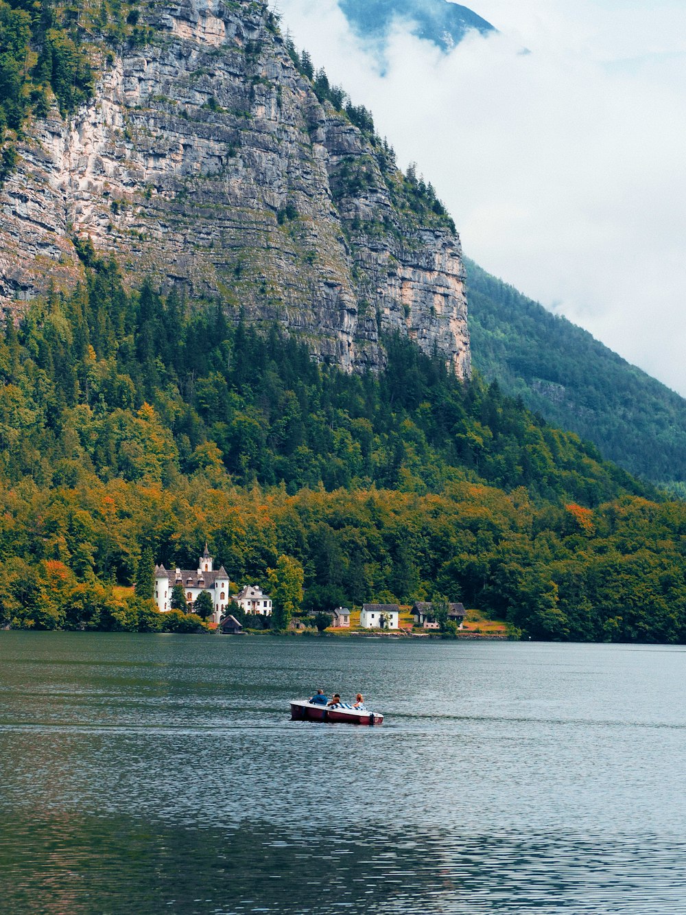 white and red boat on body of water near green mountain during daytime