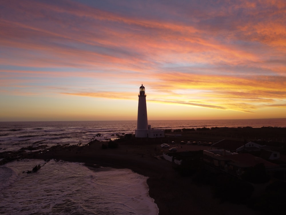 white and black lighthouse on brown sand during sunset