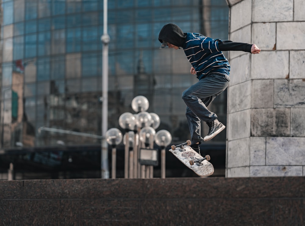 uomo in camicia a maniche lunghe a righe blu e bianche e pantaloni neri che cavalca lo skateboard durante il giorno
