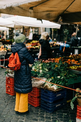 A vendor's outdoor market stall table set up with baskets of fresh produce and handmade goods under a canopy tent