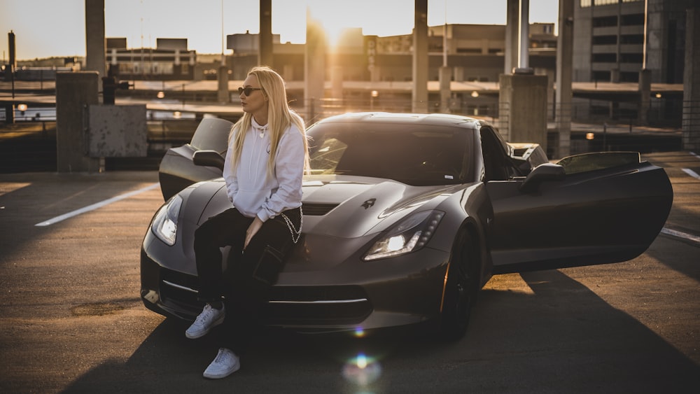 Femme en chemise blanche à manches longues et pantalon noir assise sur une voiture noire