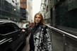 A stylish woman wearing a fitted leather jacket and jeans, standing confidently on a city street.