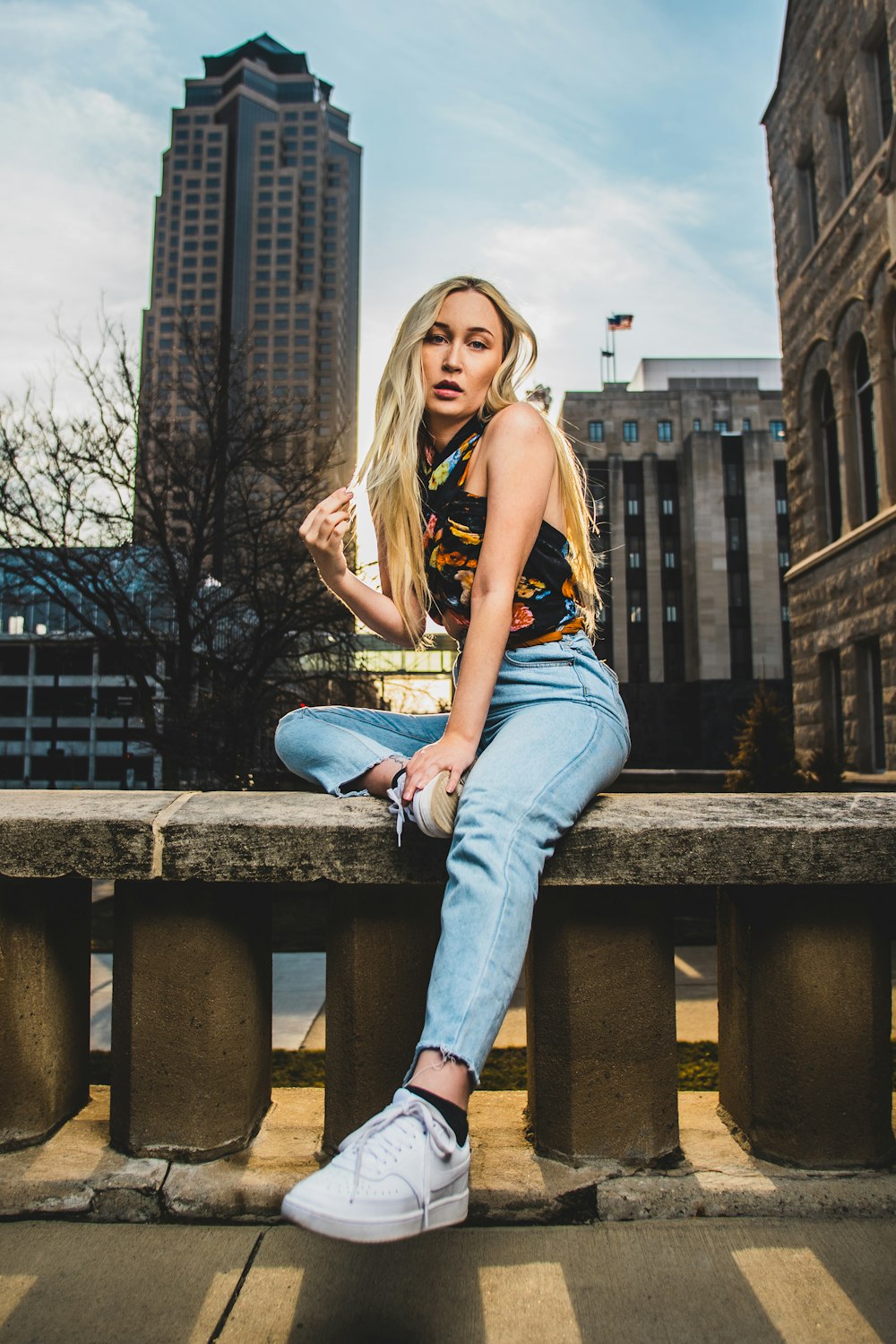 woman in yellow and black tank top and blue denim jeans sitting on brown wooden bench