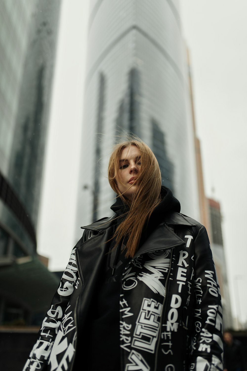 woman in black leather jacket standing near white wall during daytime