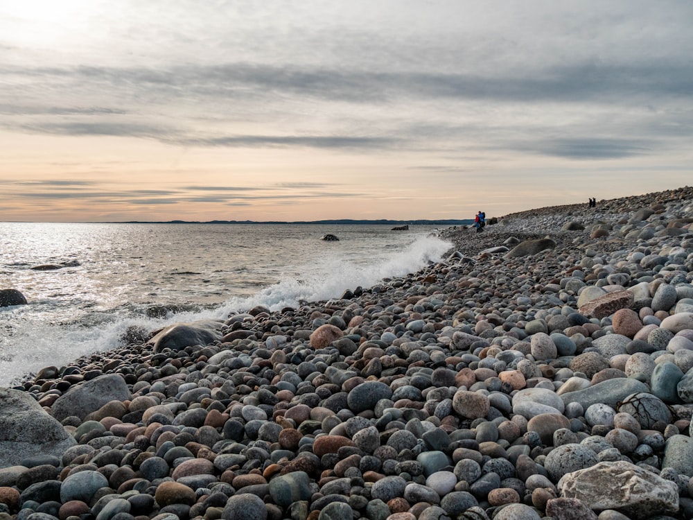 person in blue shirt standing on rocky shore during daytime