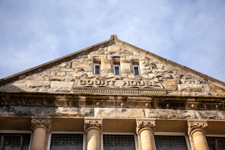 A historic stone building facade with the words 'Court House' carved into it. The structure features classical architectural elements, including ornate columns and detailed stonework, with a clear blue sky in the background.