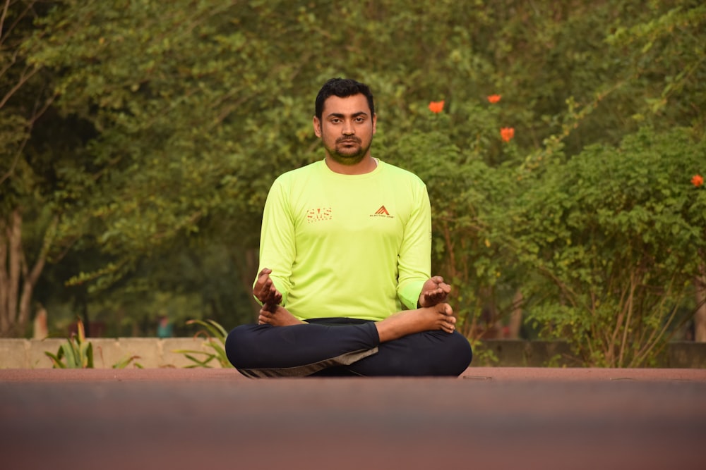 man in yellow crew neck t-shirt and black pants sitting on brown concrete floor during