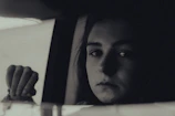 Black and white portrait of a thoughtful person looking out through a rain-speckled window.