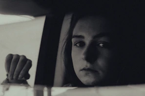 Black and white portrait of a thoughtful person looking out through a rain-speckled window.