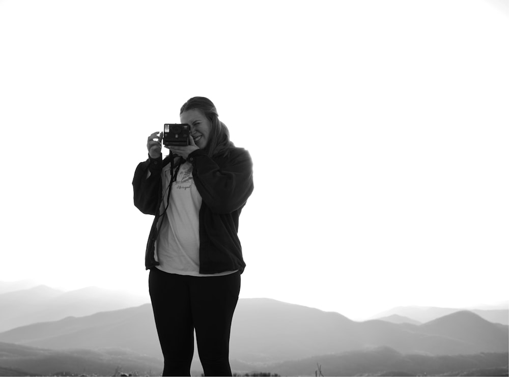 woman in white jacket taking photo of mountain