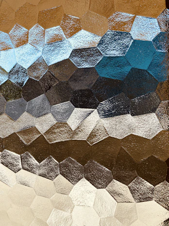 An elegant close-up of interlocking hexagonal patterns with ocean waves subtly reflected in metallic silver and warm gold hues.