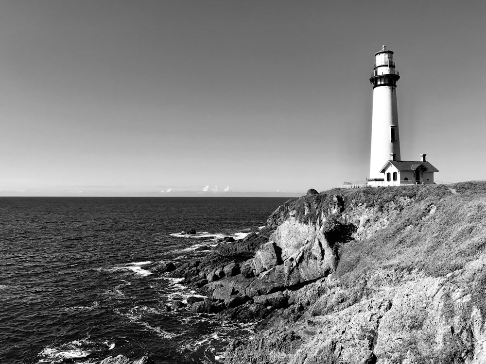 grayscale photo of lighthouse near body of water