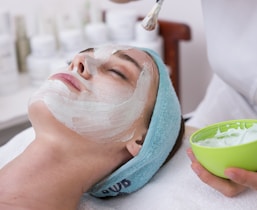 woman lying on blue towel with white cream on face