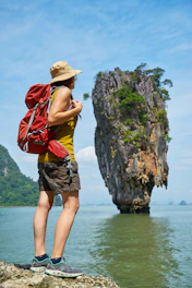 woman in yellow and red tank top and brown shorts standing on rock formation near body