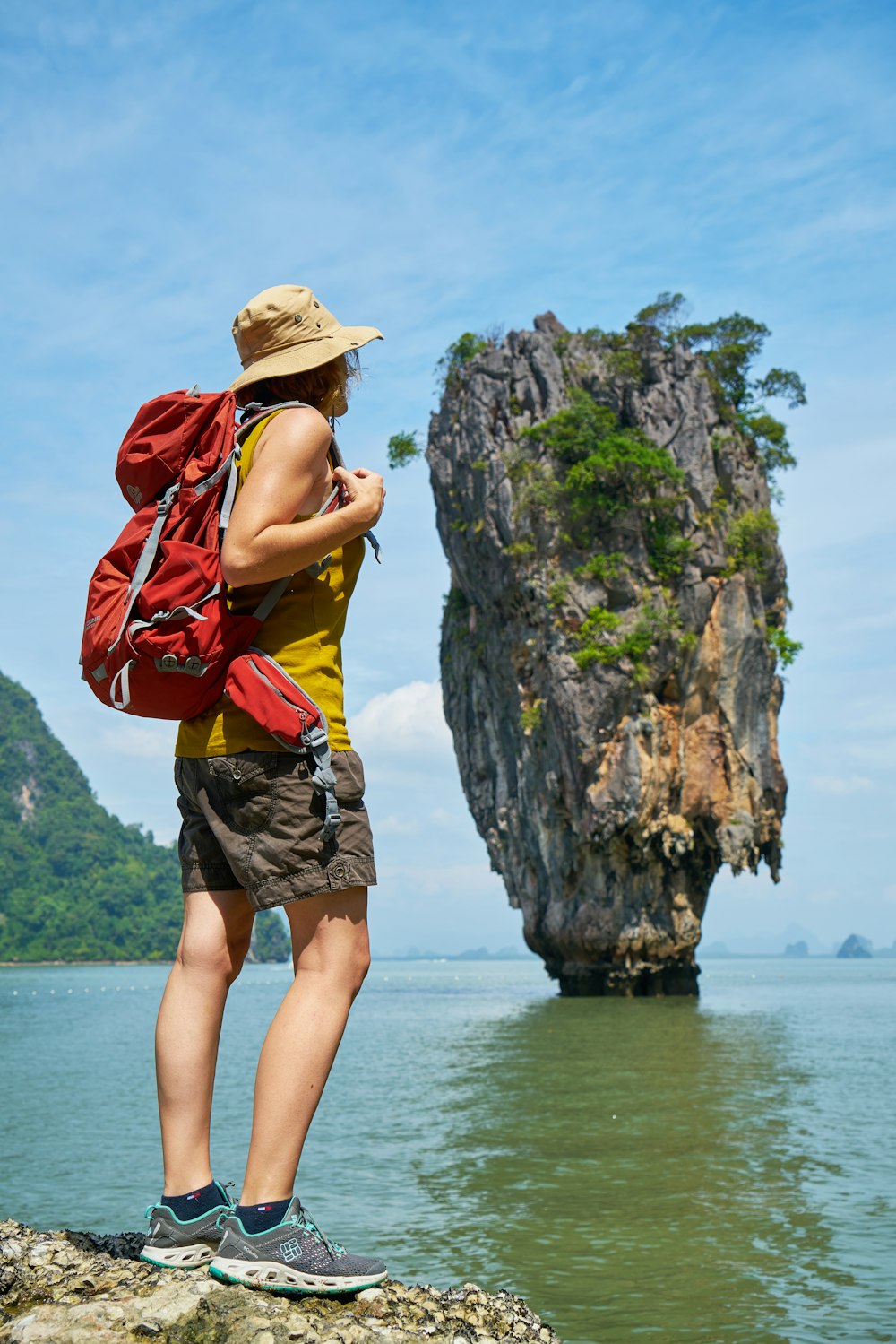 woman in yellow and red tank top and brown shorts standing on rock formation near body