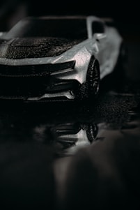A sleek black vehicle gleaming under soft light, reflecting water droplets on its polished surface.