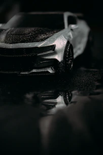 A sleek black car gleaming after a meticulous exterior wash and polish on a dark, moody backdrop.