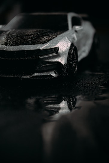 A sleek black vehicle gleaming under soft light, reflecting water droplets on its polished surface.