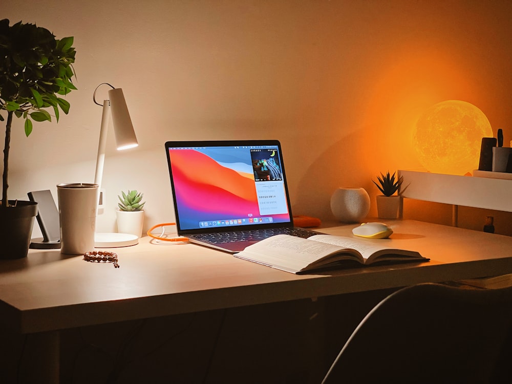 A refurbished Apple Macbook being used on a desk with a open book and other ornaments